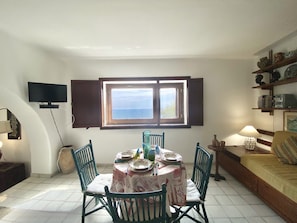 Un coin repas avec une table dressée pour quatre personnes, un téléviseur fixé au mur et une fenêtre donnant sur la mer.