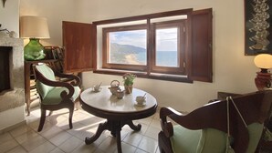 Una habitación con una mesa redonda, dos sillas, una estantería, una lámpara y una ventana con vista al mar.