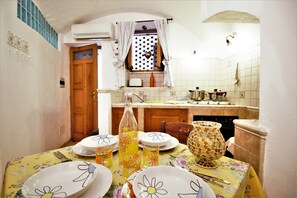 Un comedor con una mesa dispuesta para cuatro, una ventana con cortinas y una cocina al fondo.