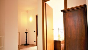 Un pasillo con puerta de madera, una mesita con lámpara y suelo de baldosas.