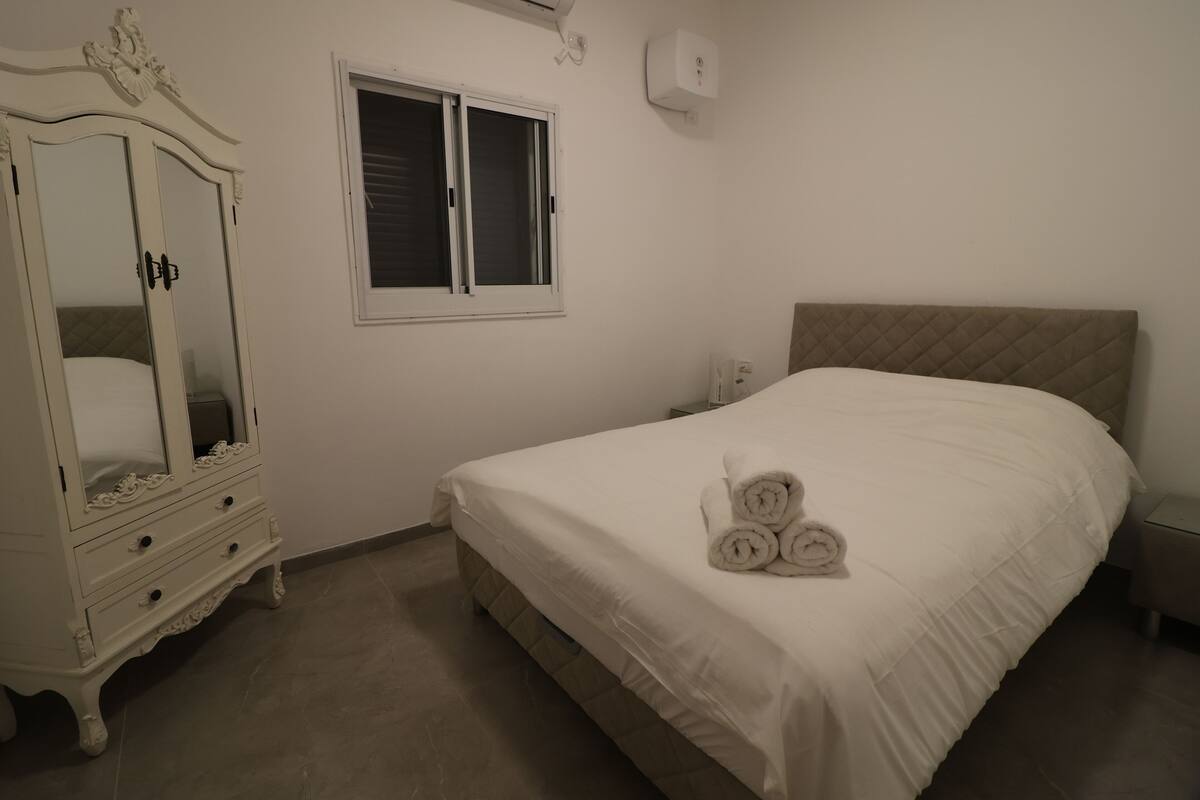 A bedroom with a bed, a dresser, a window, and a wall-mounted air conditioner.