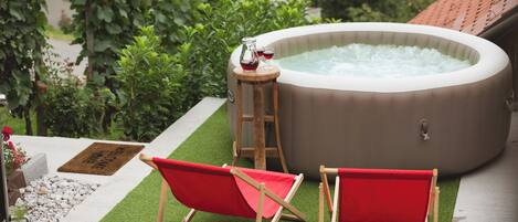Ein Whirlpool mit zwei roten Stühlen, umgeben von Grünpflanzen und einem kleinen Tisch mit Getränken.