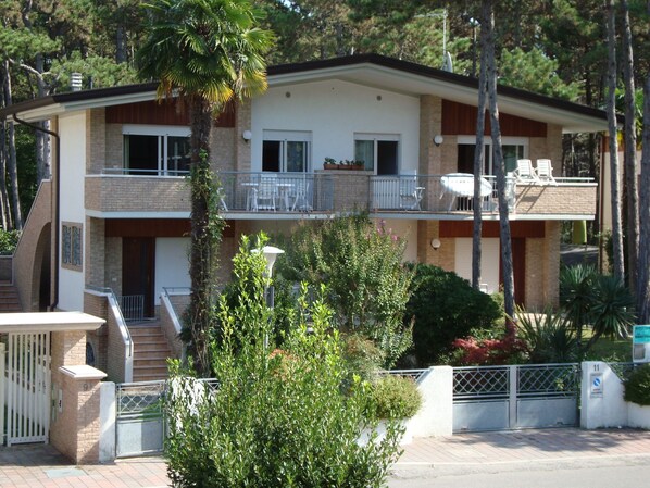A two-story building with a balcony on the upper floor, a gated entrance, and a small garden area. - Villa Anny apartment 1 (Lignano Sabbiadoro)