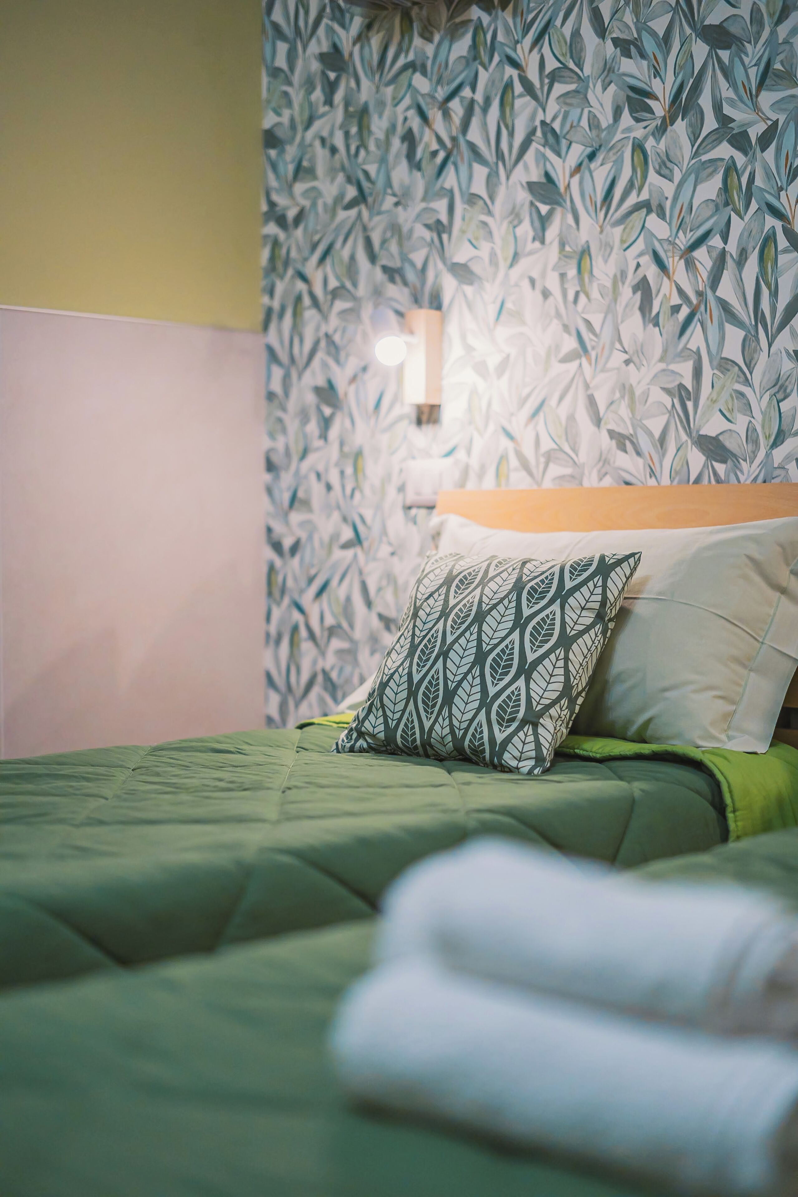 A neatly made bed with a green bedspread, a patterned pillow, and a plain pillow.