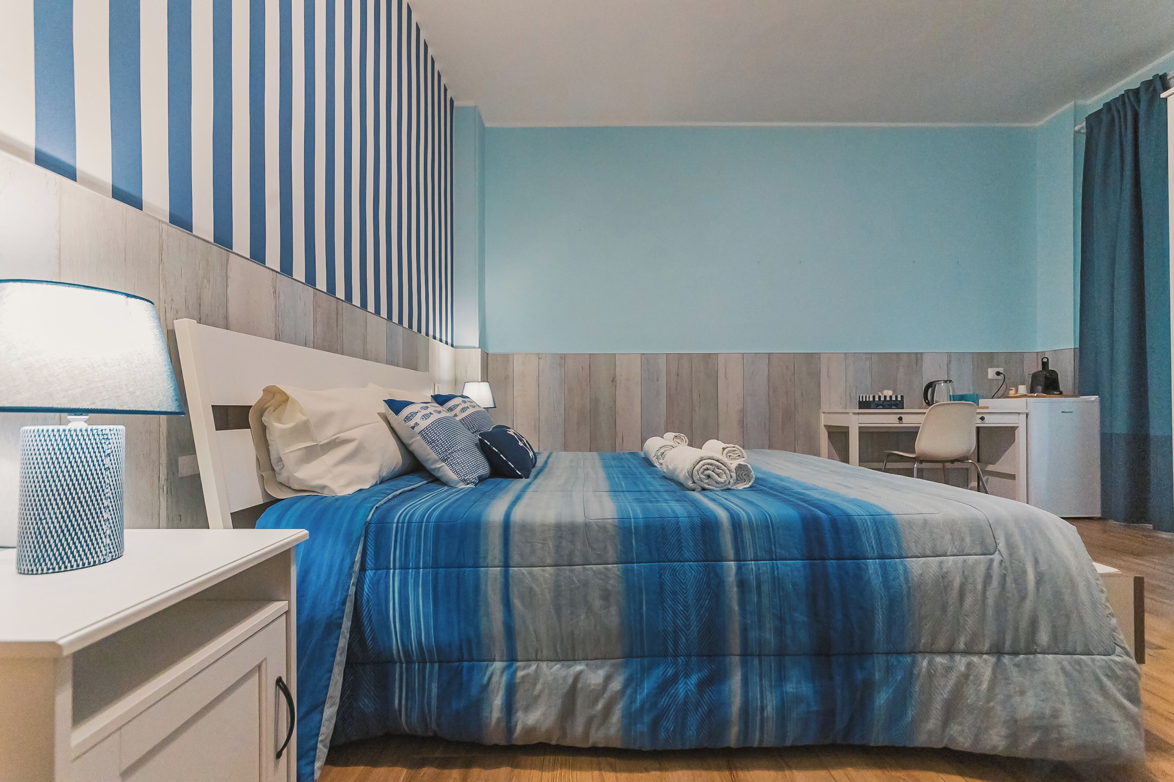 A bedroom with a bed, bedside table, lamp, and a desk with a chair.