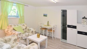 Une pièce comprenant un canapé, une petite table, une table à manger avec des chaises, un réfrigérateur et une fenêtre avec des rideaux.