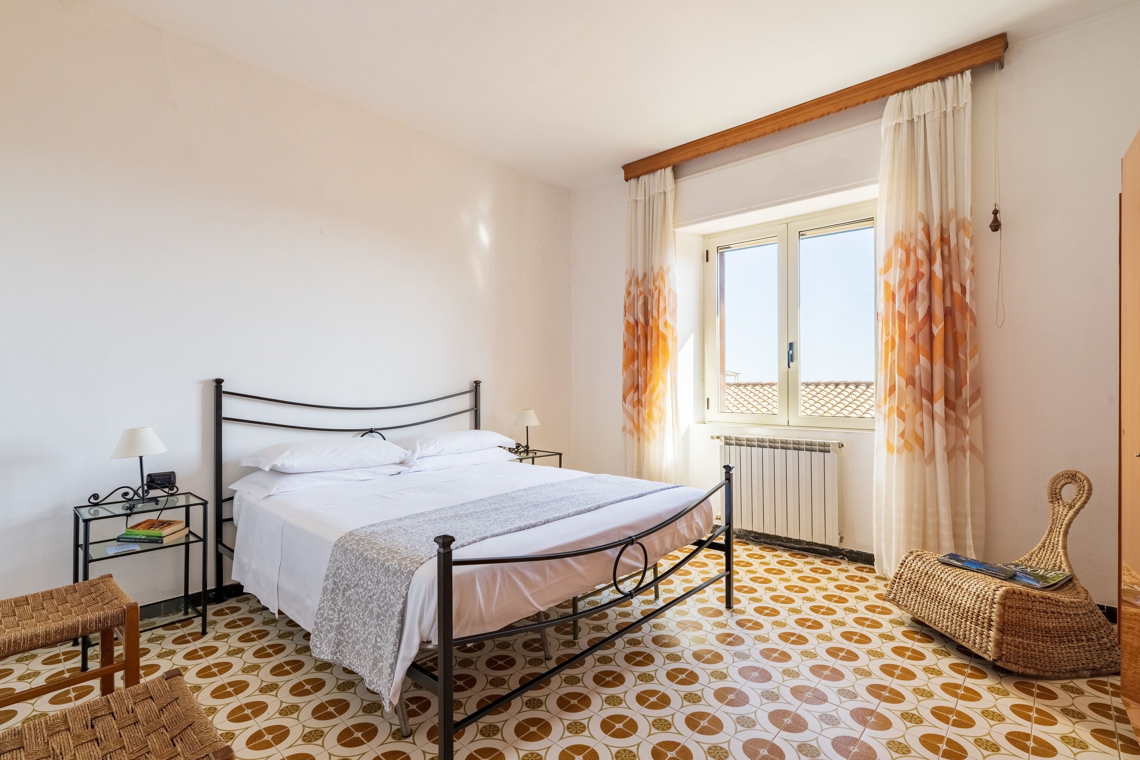 Une chambre à coucher avec un lit, une table de chevet, une lampe et une fenêtre avec des rideaux.