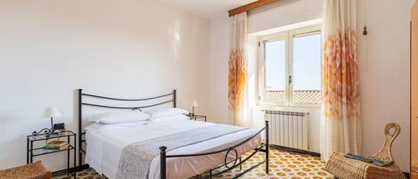 Une chambre à coucher avec un lit, une table de chevet, une lampe et une fenêtre avec des rideaux.