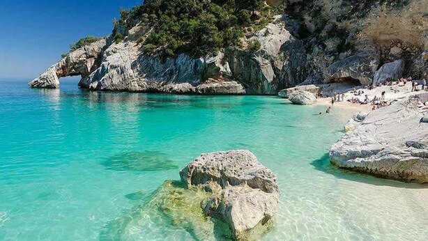 A coastal beach with clear turquoise water, rocky formations, and a small crowd of people. - SANTA MARIA NAVARRESE WITH GARDEN AND SEA VIEW (Baunei)