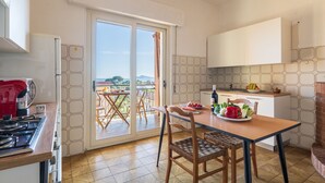 A modern kitchen with a dining area, a view through a glass door, and a red kettle on the stove. - SANTA MARIA NAVARRESE WITH GARDEN AND SEA VIEW (Baunei)
