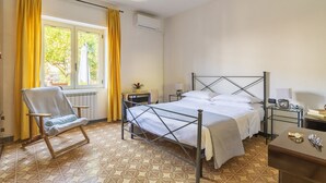 A bedroom with a metal-framed bed, a chair, a bedside table, and a window with curtains. - SANTA MARIA NAVARRESE WITH GARDEN AND SEA VIEW (Baunei)