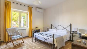 A bedroom with a metal-framed bed, a chair, a bedside table, and a window with curtains.