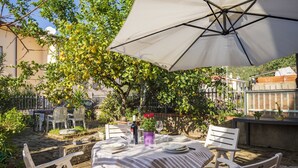 An outdoor dining area with a table set for two under a large umbrella, surrounded by greenery and a stone wall. - SANTA MARIA NAVARRESE WITH GARDEN AND SEA VIEW (Baunei)