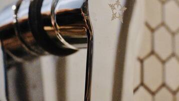 A chrome faucet with a visible brand logo, set against a tiled wall with a honeycomb pattern.