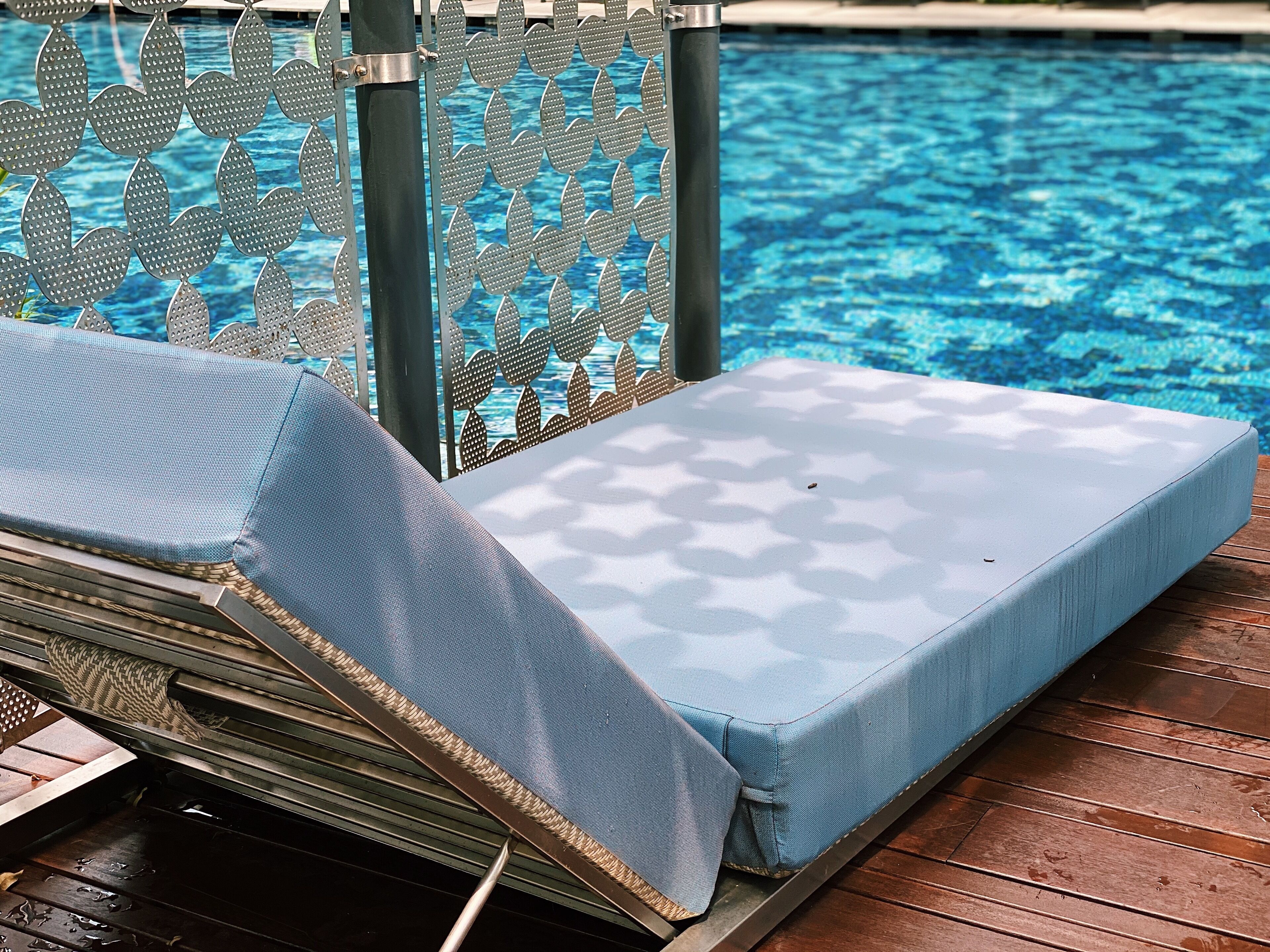 A poolside lounge area with a metal fence and a cushioned lounge chair.