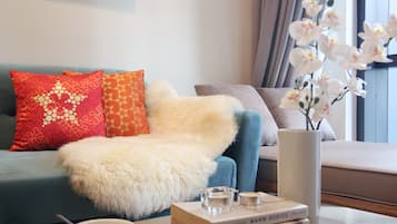 A modern living room with a blue sofa, white fluffy throw, and a vase with white orchids.