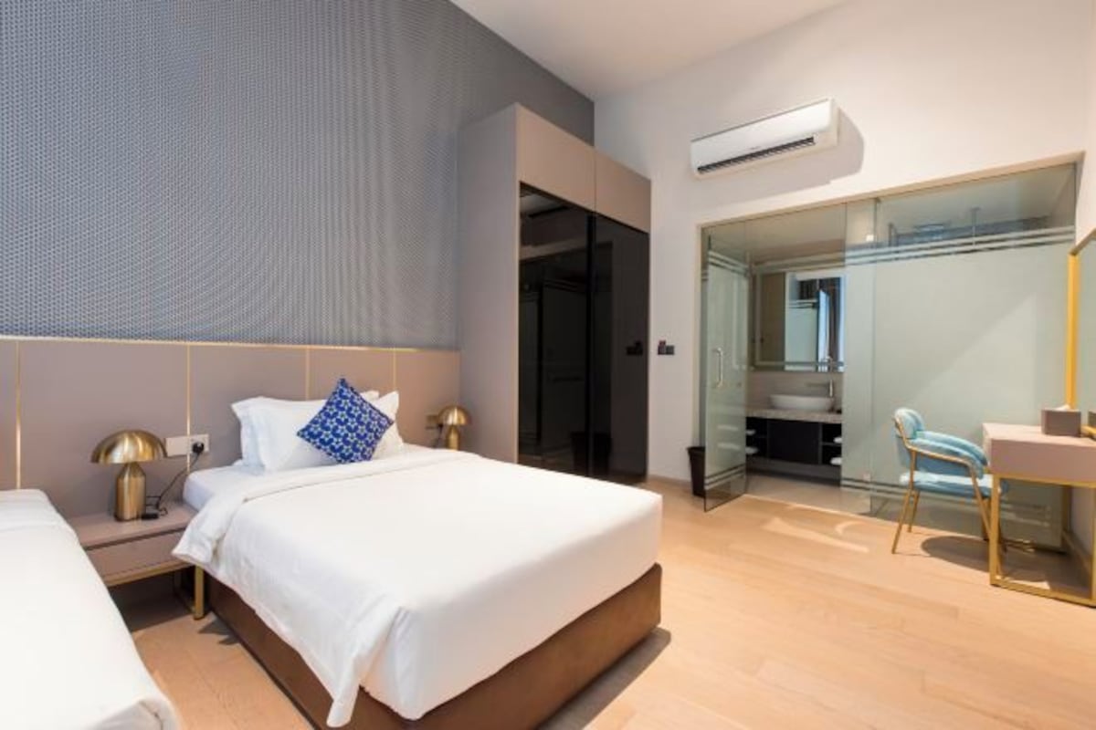 Una habitación de hotel moderna con una cama grande, mesitas de noche, un escritorio y un baño con mampara de vidrio.