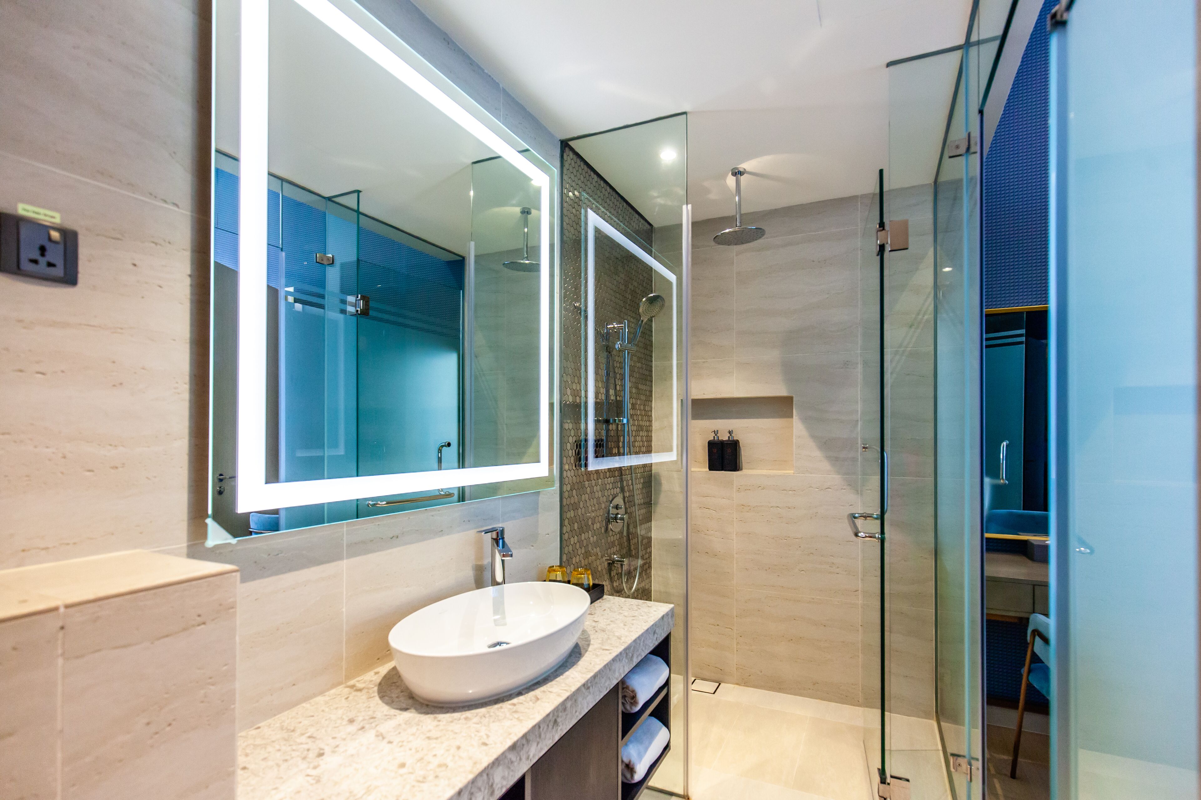 A modern bathroom with a large mirror, a round sink, and a glass-enclosed shower area.