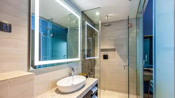 Une salle de bain moderne avec un grand miroir, un lavabo rond et une douche séparée par des parois en verre.