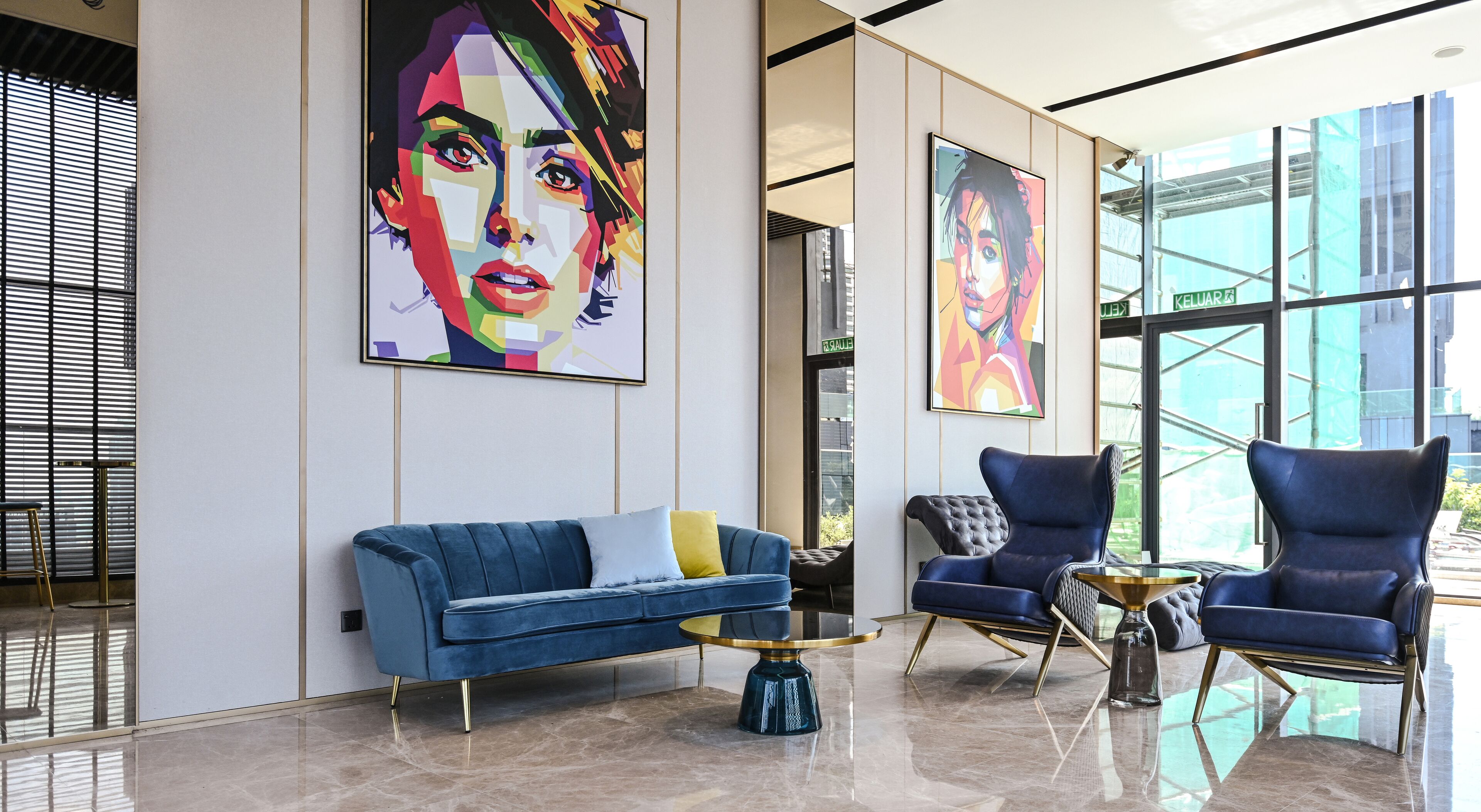 Eine moderne Lobby mit einem blauen Sofa, einem runden Couchtisch und zwei Sesseln. Große Fenster und Kunstwerke schmücken die Wände.