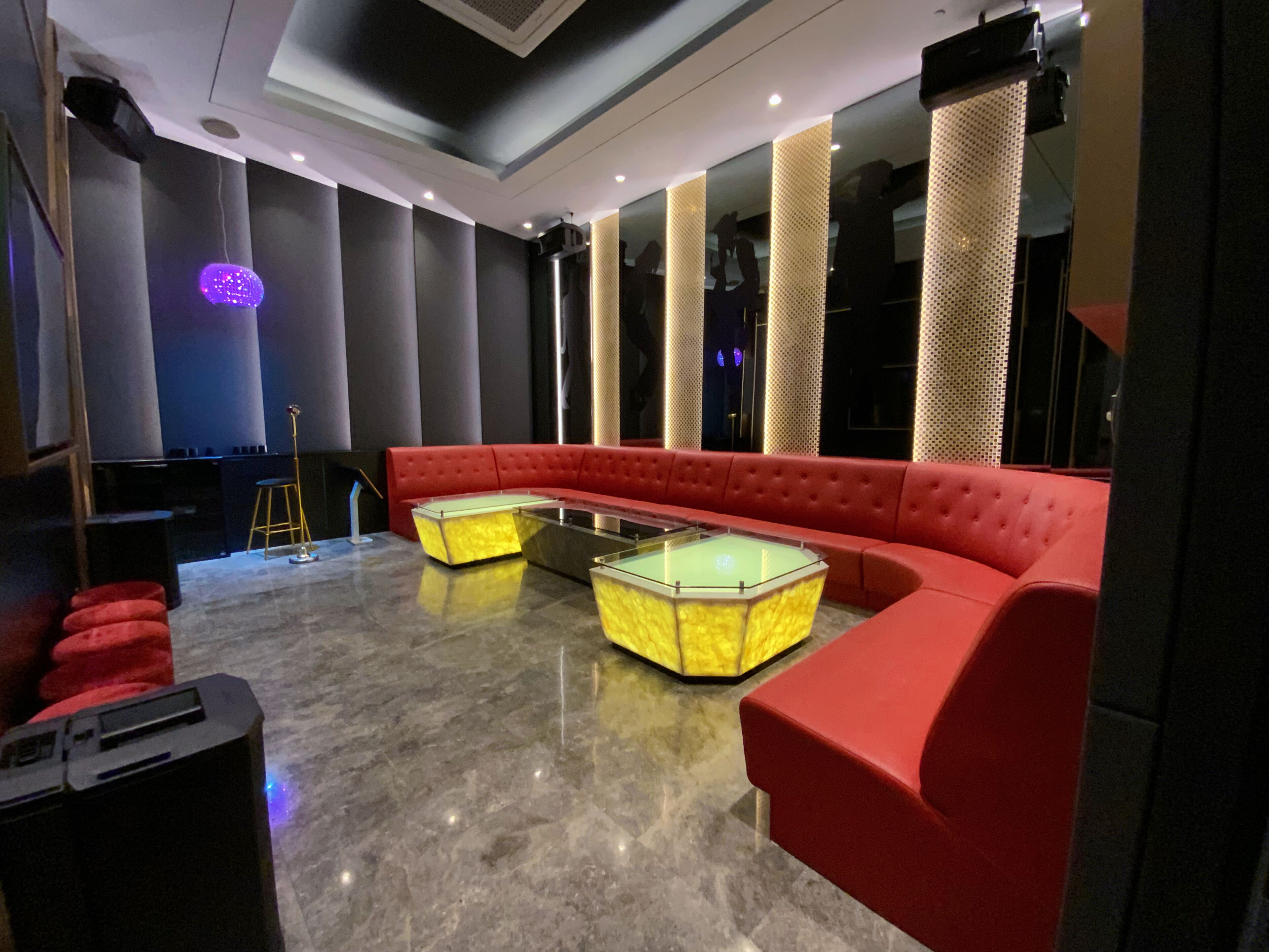 Eine moderne Lounge mit einem roten Sofa, zwei Tischen mit Glasplatten und einer Bühne mit violetter Beleuchtung.