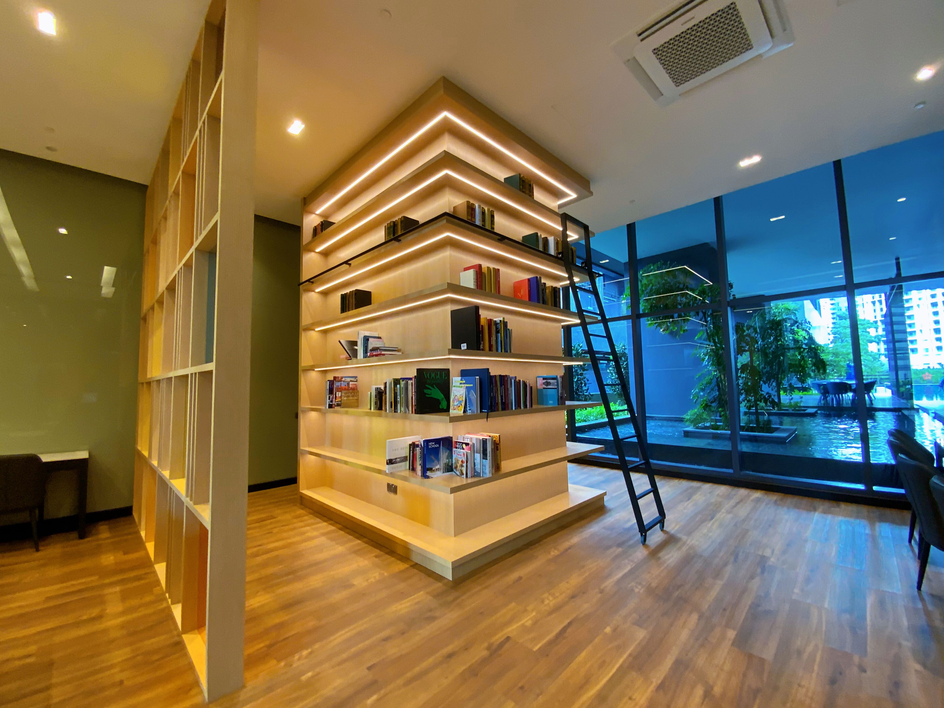 A modern interior with a wooden bookshelf, a ladder, and a view of a water feature outside.