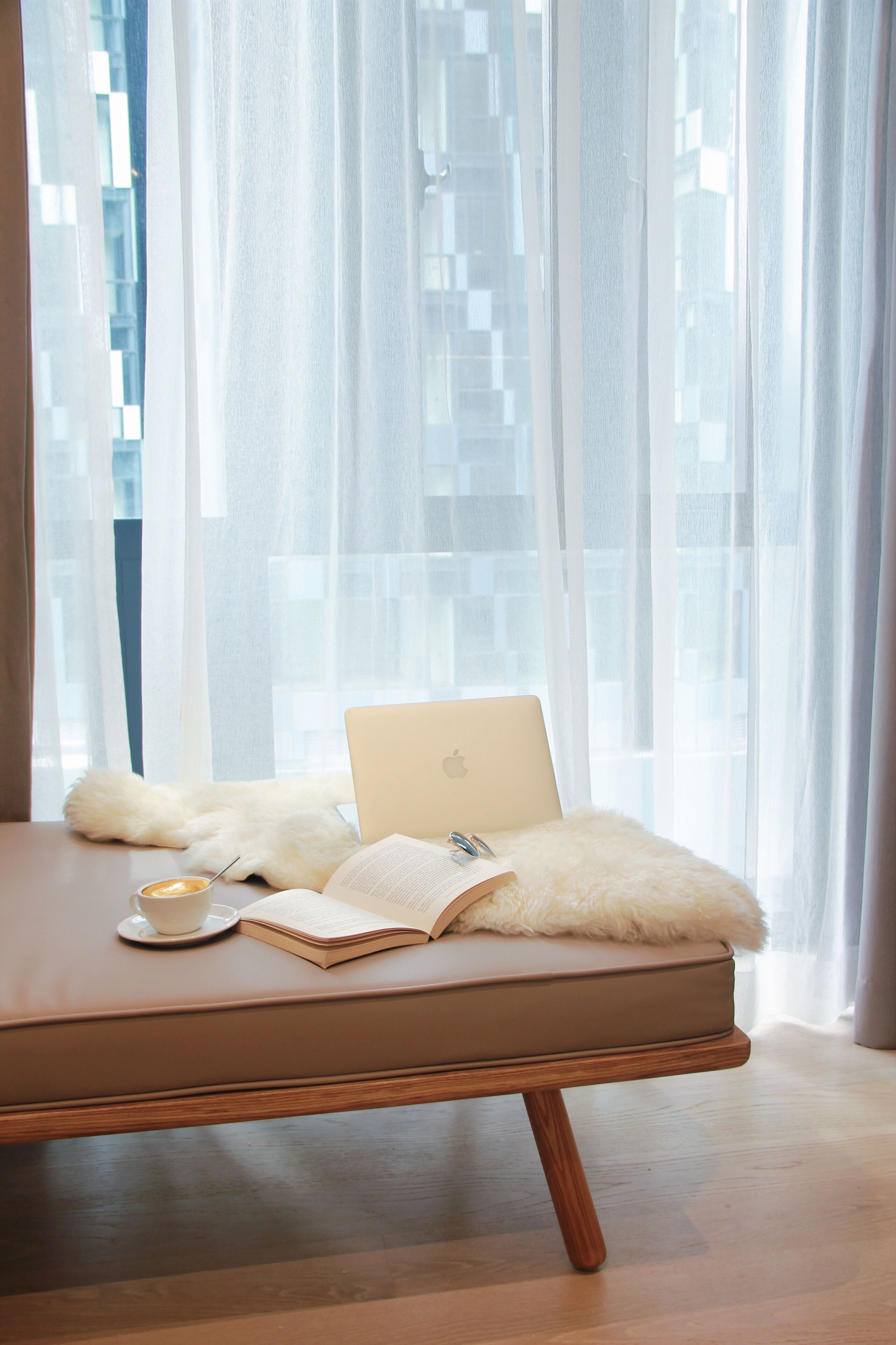 A modern room with a laptop on a cushioned bench, a book, and a cup on a saucer.