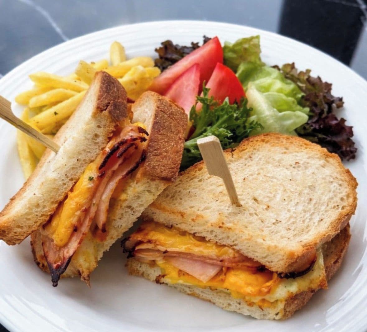 A sandwich with a toothpick, accompanied by a side of fries and a salad.
