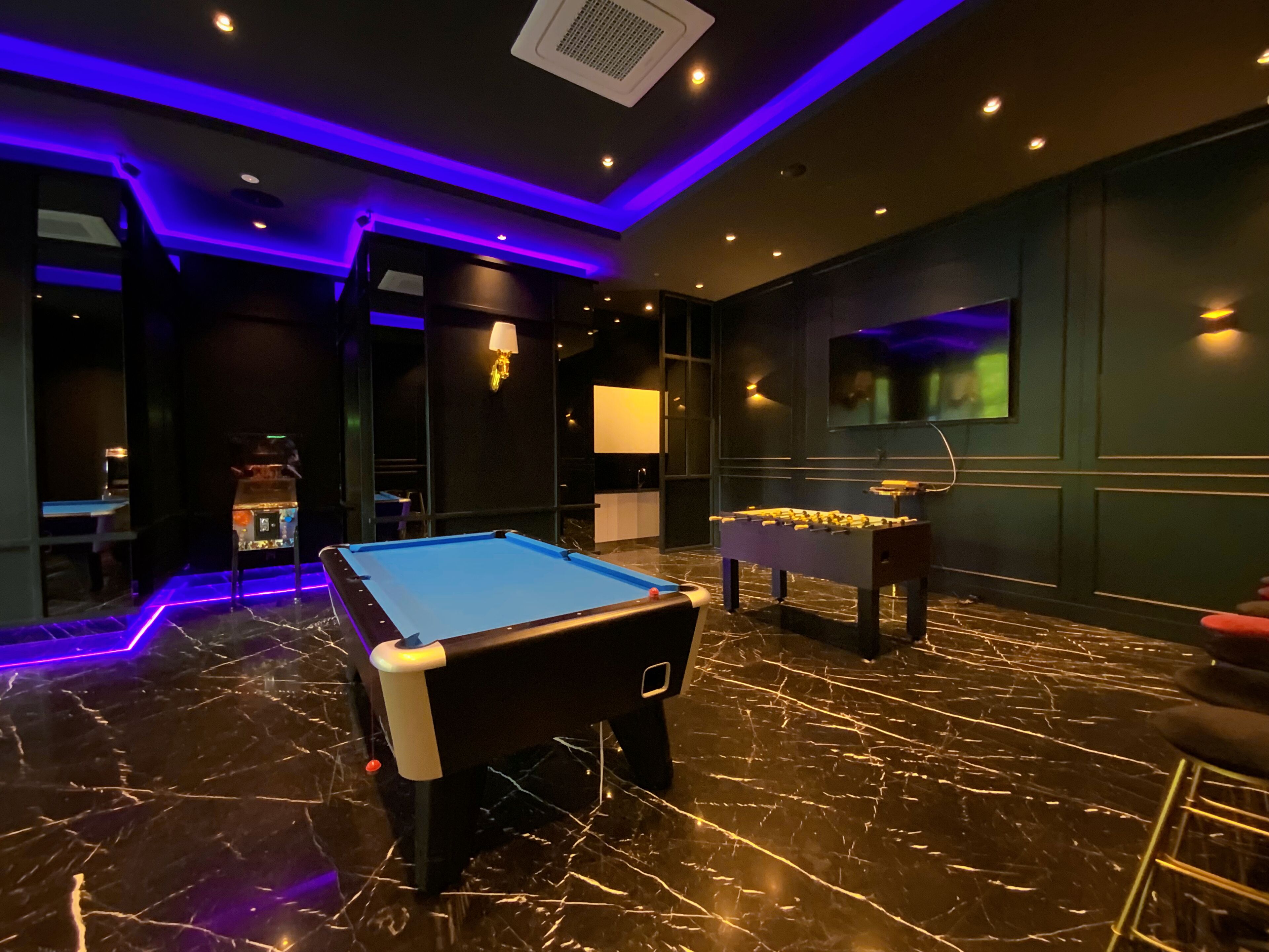 A billiards room with a pool table, foosball table, and a bar area.