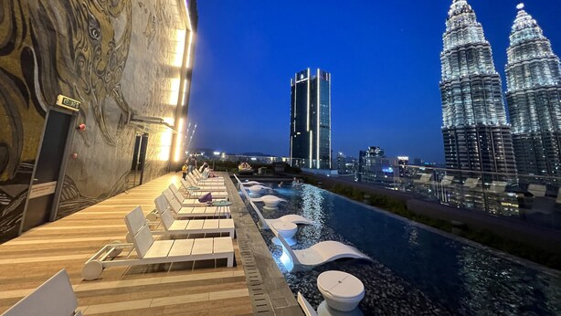 Un espace piscine aménagé sur le toit, avec des chaises longues et une vue sur les tours Petronas.