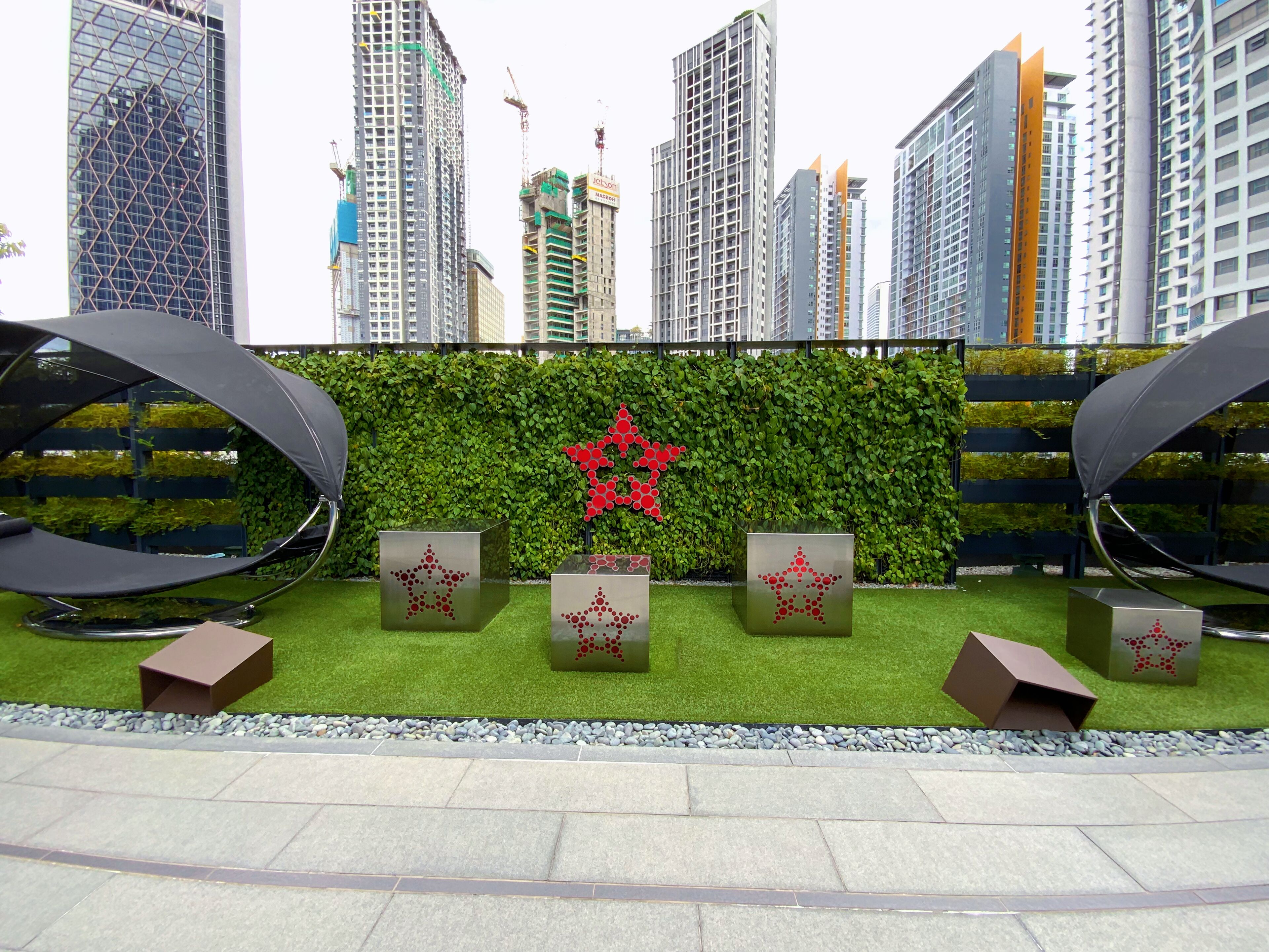 A modern outdoor seating area with a green hedge backdrop and a red star decoration.