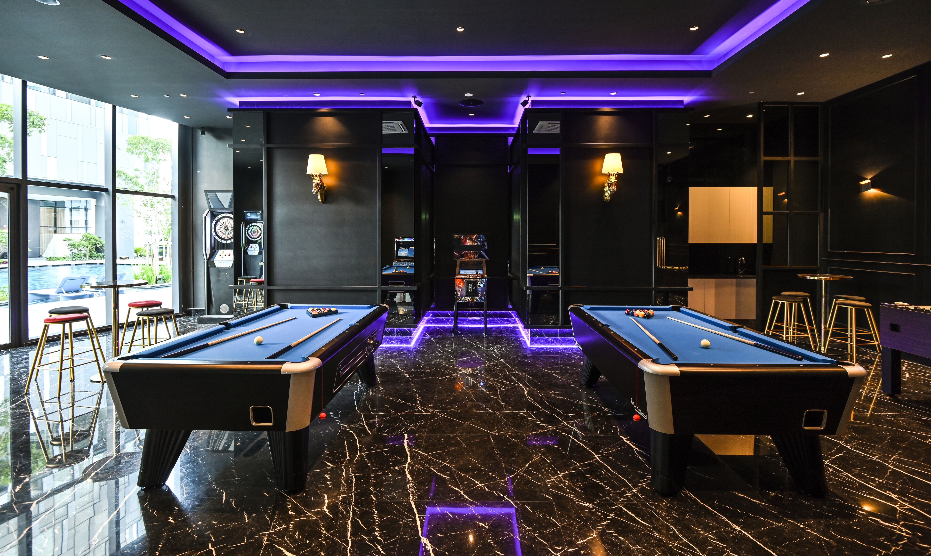 Ein Billardraum mit zwei Billardtischen, einer Bar und Blick auf einen Pool.