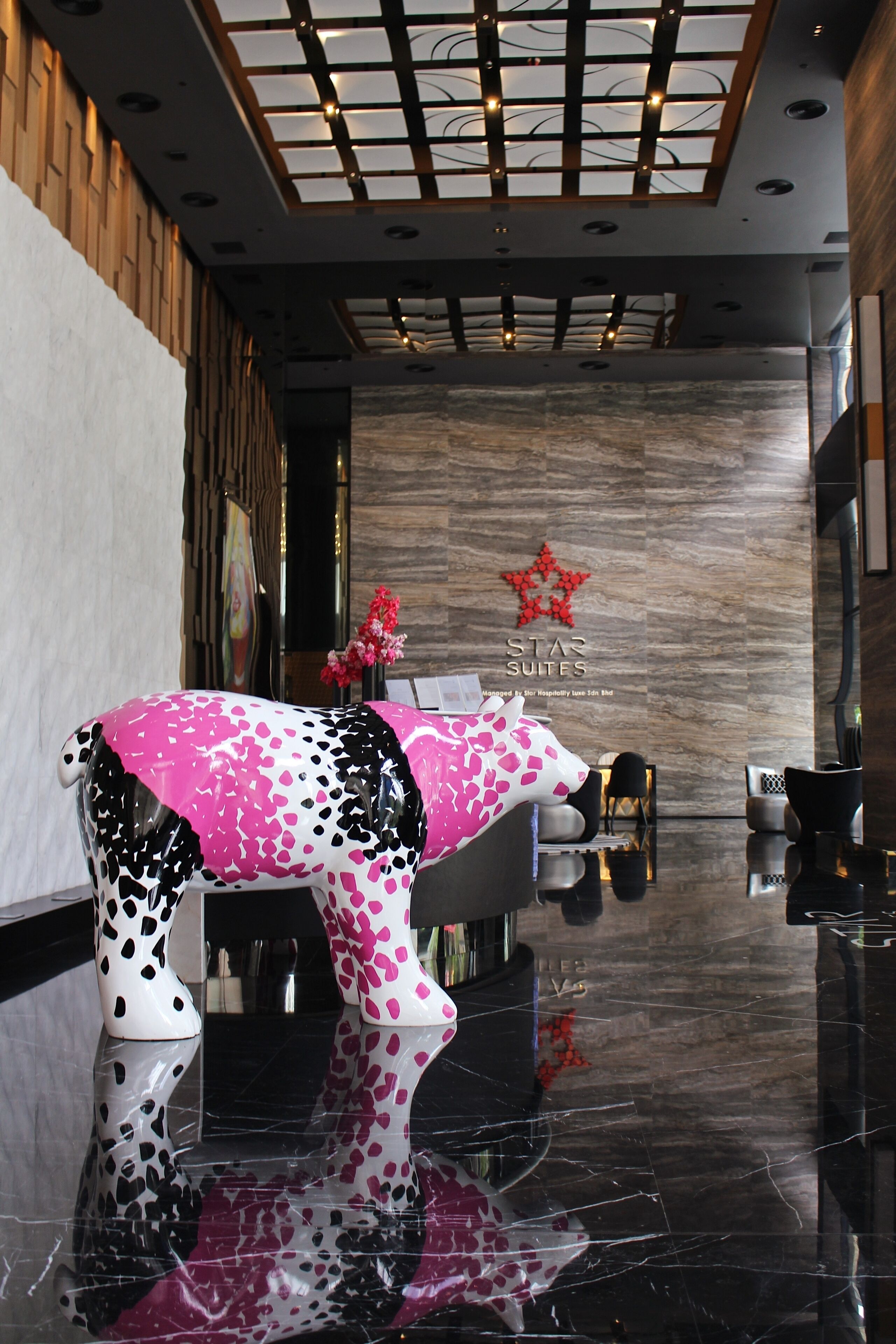 A modern hotel lobby with a reflective floor, a reception desk, and a decorative cow sculpture.