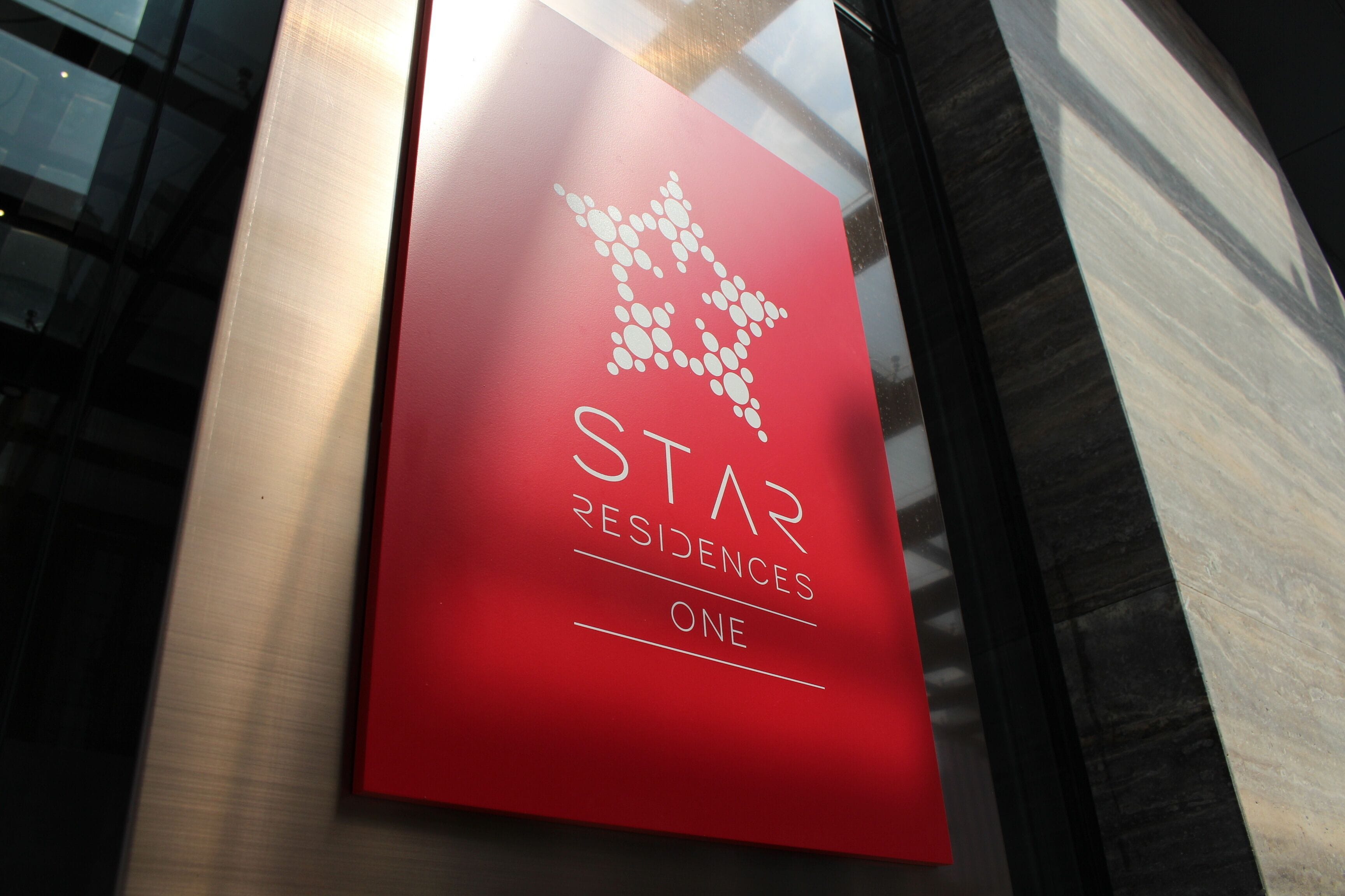 Un panneau rouge avec l’inscription « STAR RESIDENCES ONE » et un motif stylisé d’étoile.