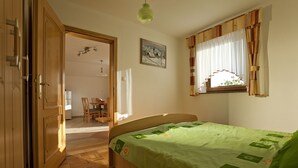Een slaapkamer met een houten bed, een raam met gordijnen, een schilderij aan de muur en een deur naar een andere kamer.
