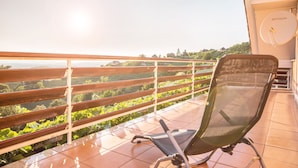 Un balcon avec une chaise, une antenne parabolique et une vue sur un paysage verdoyant.