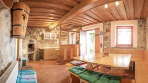 Une cuisine rustique avec un mur en pierre, des armoires en bois, une grande table en bois et un banc agrémenté de coussins verts.