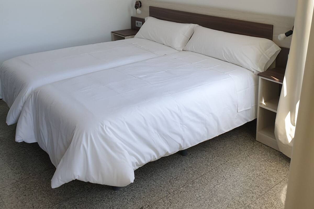 Una cama doble con ropa de cama blanca en una habitación de hotel.