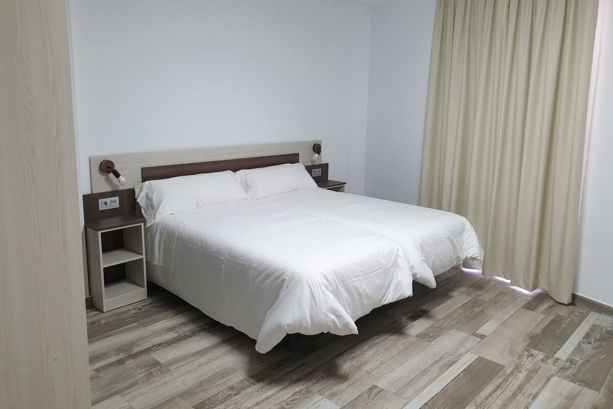Una cama bien tendida con un cabecero de madera y una mesita de noche con una lámpara.