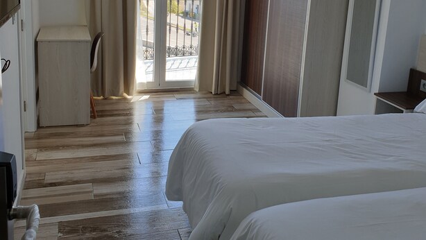 Una habitación de hotel con dos camas, piso de madera, balcón con vistas y un armario.