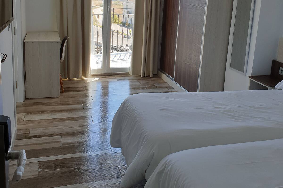 Una habitación de hotel con dos camas, piso de madera, balcón con vistas y un armario.