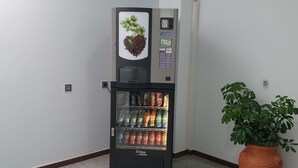 Una máquina expendedora con diseño de taza de café, una planta en maceta y un letrero de salida verde en la pared.