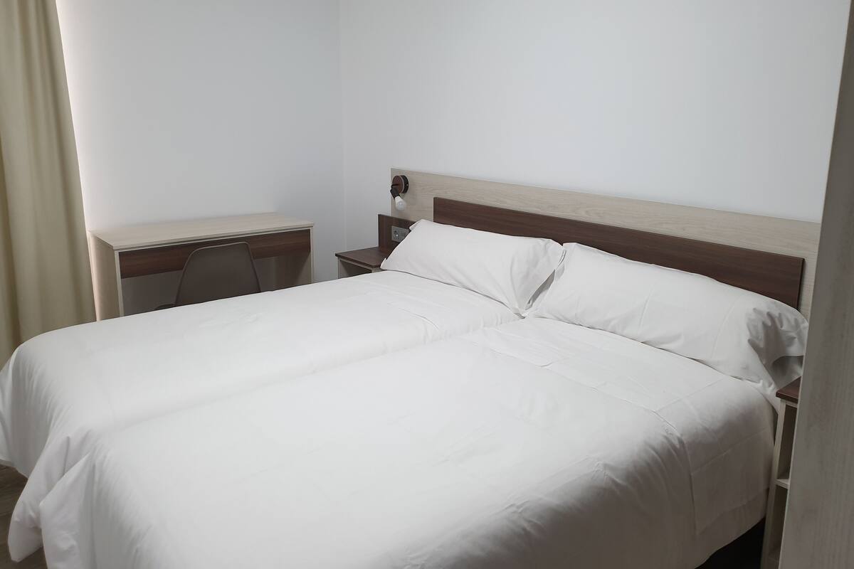 Una habitación de hotel con una cama individual, una mesita de noche de madera, un escritorio y una silla.