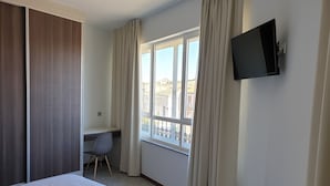 Habitación de hotel con cama, escritorio, silla, televisor montado en la pared y ventana con cortinas.