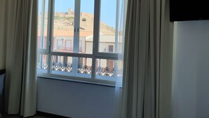 Una habitación con un ventanal grande, cortinas blancas y un televisor montado en la pared.