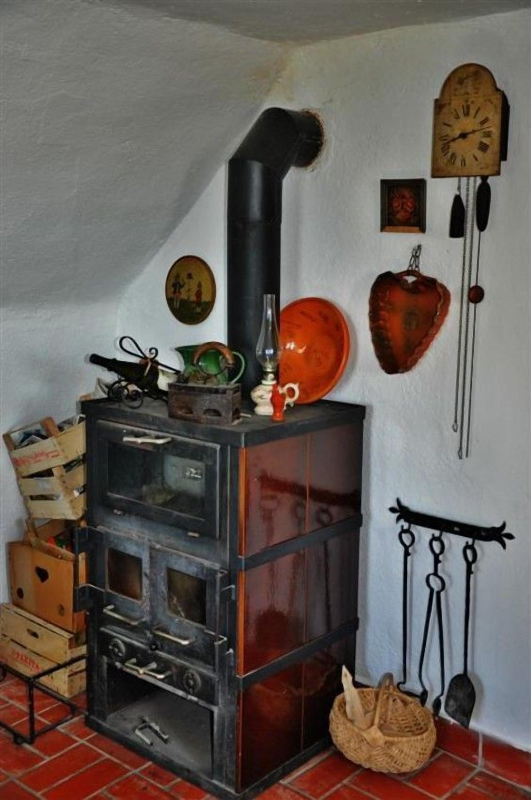 A traditional wood-burning stove with a chimney, a clock, and various kitchen utensils on the wall.