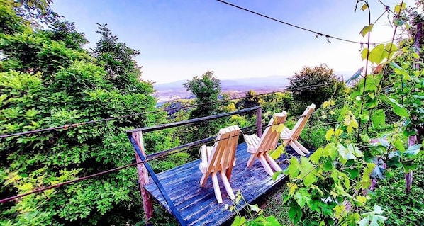 A wooden platform with easels and a metal railing overlooking a lush garden and distant landscape.