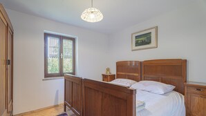 A bedroom with a wooden bed, a nightstand, a window with a view, and a hanging light fixture. - Vineyard cottage Vrbekova gorca (Šmarje pri Jelšah)