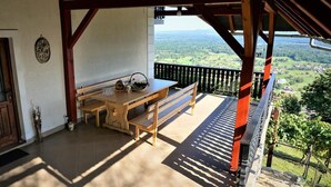 A wooden table and bench on a balcony with a view of a green landscape. - Vineyard Cottage Zajc (Semic)