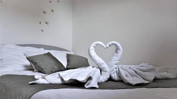 A bed with a white and gray blanket, two pillows, and a heart-shaped towel arrangement on the bed. - Vineyard Cottage Zajc (Semic)